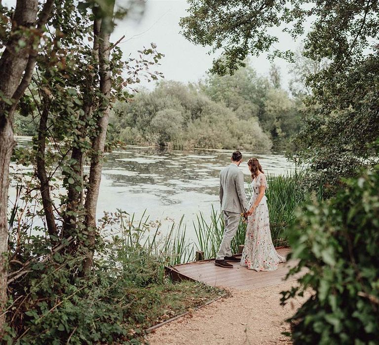 Bride in floral embroidered wedding dress with groom in grey suit looking out over the lake