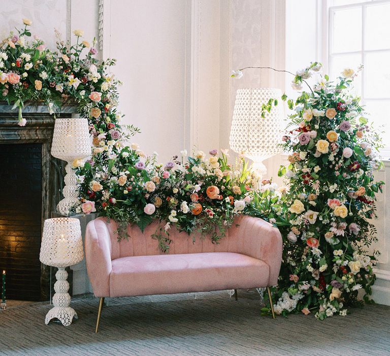 Pink velvet sofa and white lamps surrounded by colourful flower arrangements at Barnett Hill Hotel 