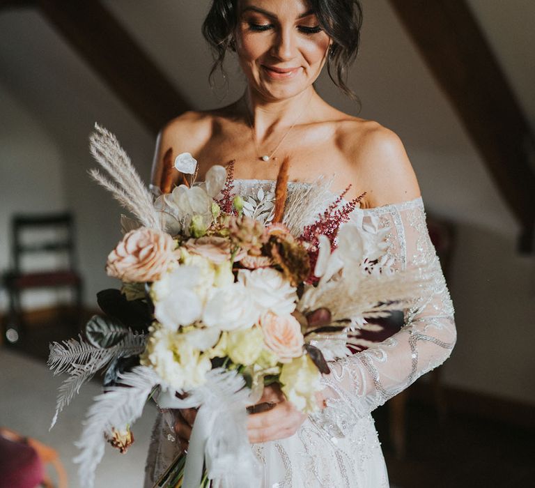 Bride in off the shoulder sparkly sequinned Zavana Couture wedding dress with light and dark flowers for her wedding bouquet