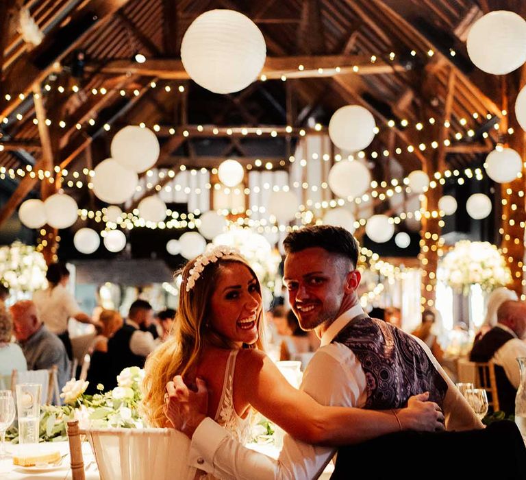 Bride and groom look back at the camera at their Cooling Castle venue wedding with white paper lantern decorations 