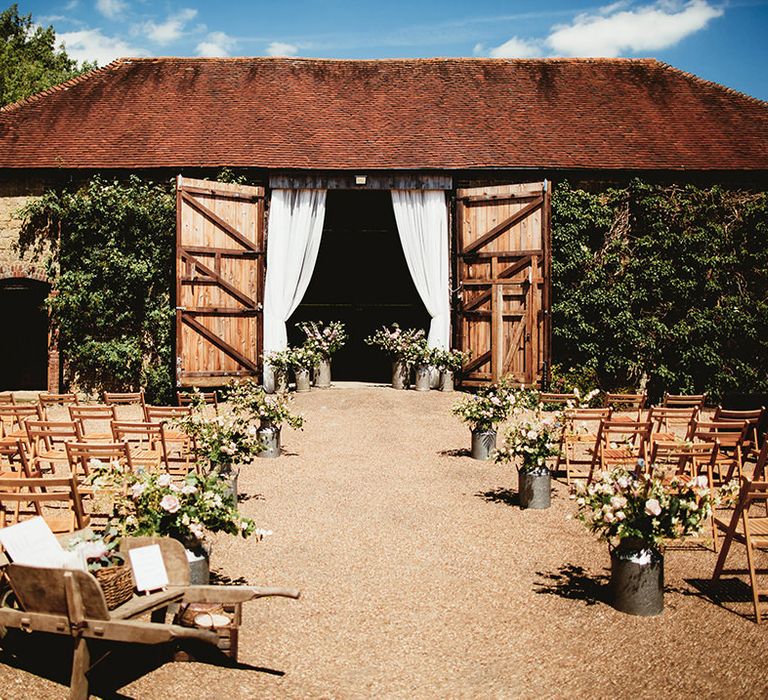 Boho South Downs National Park home wedding with vintage milk churns holding flowers for decor and wooden chairs with white drapery