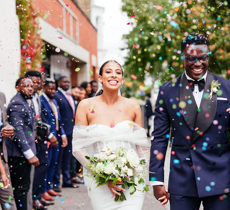 Bride and groom exit their ceremony to multi-coloured confetti at industrial city wedding venue