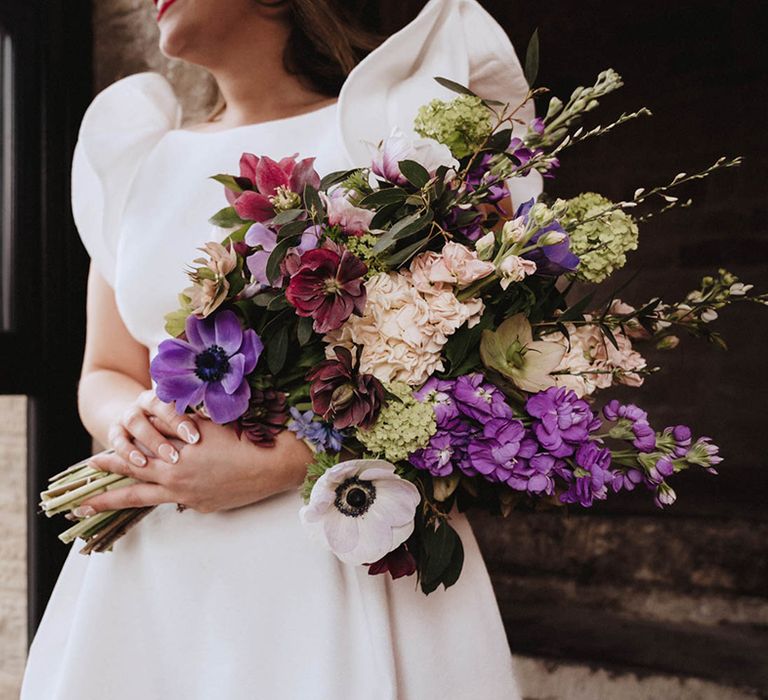 Bride with patterned abstract white nails holding onto purple, burgundy and white bouquet with stock