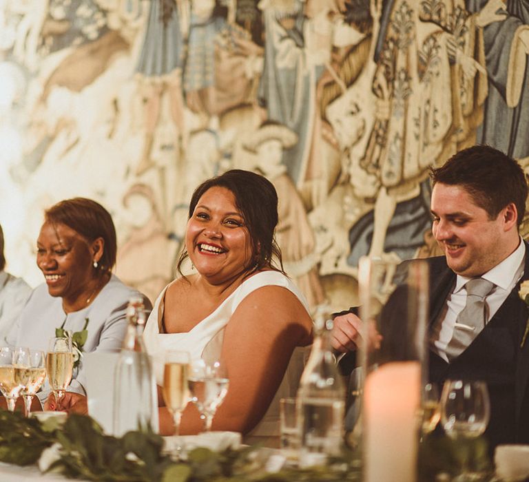 Bride, groom and other wedding guests laugh and smile during wedding speeches 