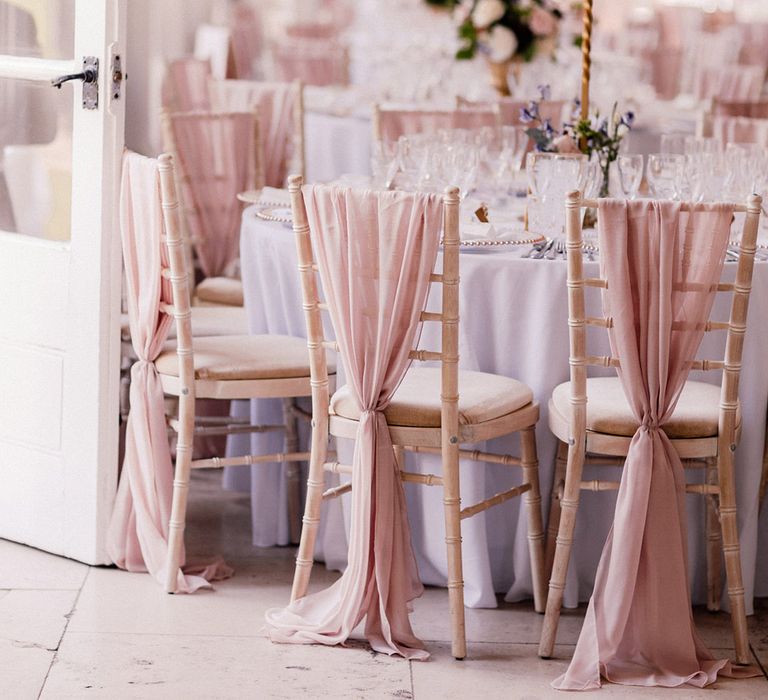 White wooden wedding chairs decorated with pink chiffon material with tables decorated with tall pink rose centrepieces 