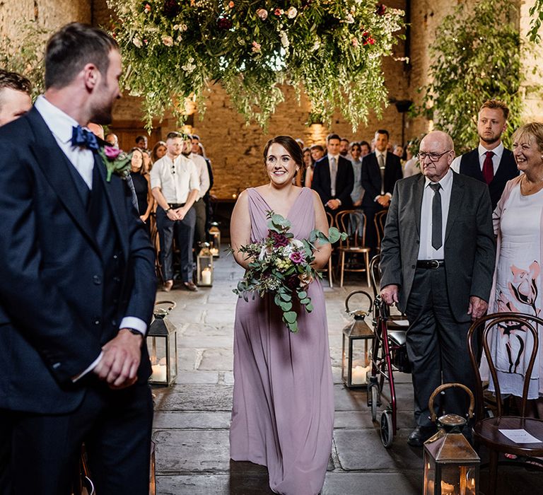 Bridesmaid in pale pink dress walks the down aisle for wedding 