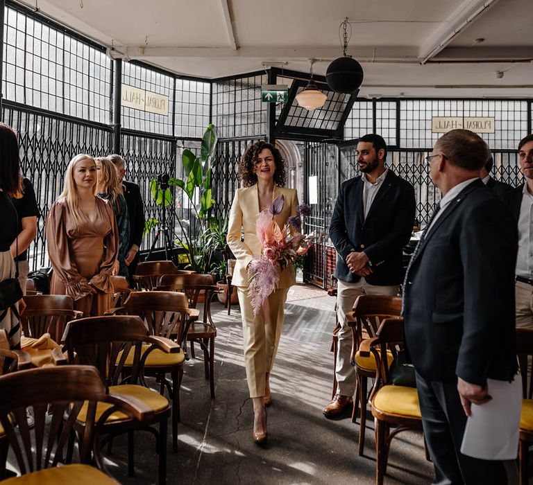 Bridesmaids in a yellow trouser suit walking down aisle at Floral Hall wedding venue 