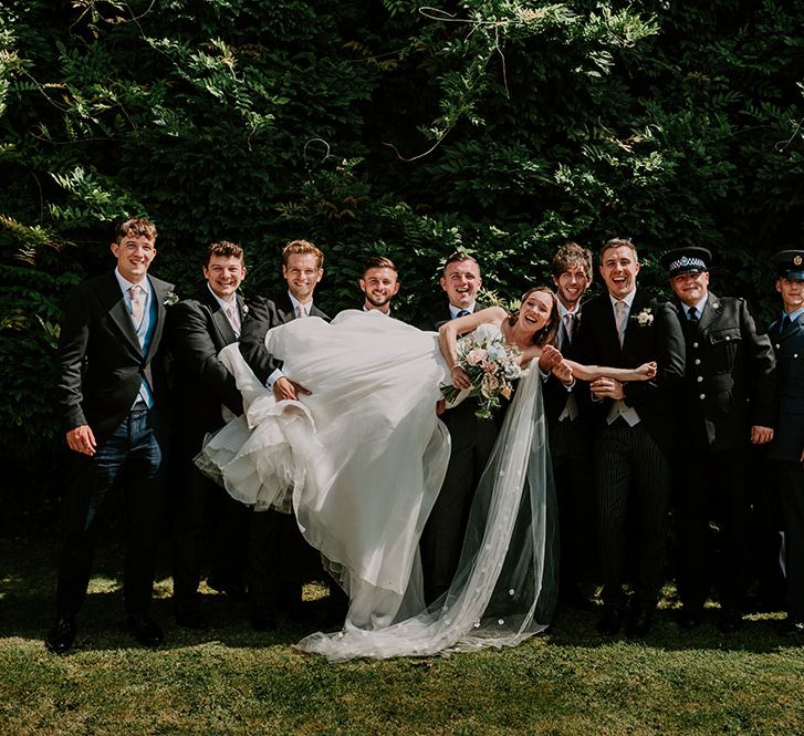 Bride is held by groom and his groomsmen outdoors for fun wedding picture 