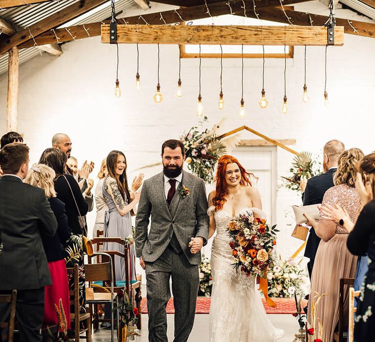 Bride and groom walk back down the aisle under festoon lighting as a married couple 