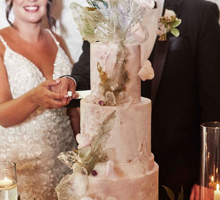 Bride in a fitted lace wedding dress and groom in a tuxedo cutting their three-tired wedding cake 