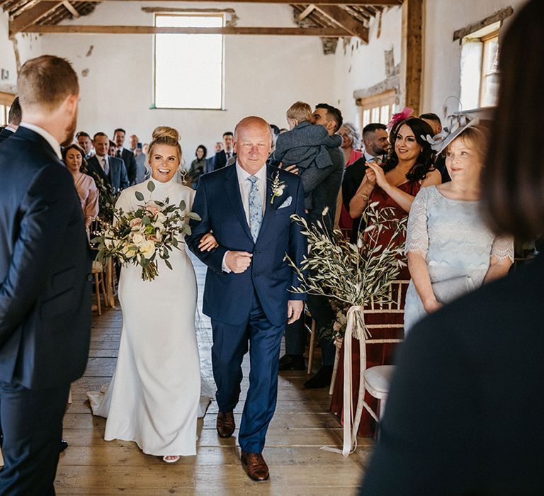 Father of the bride in a blue suit and patterned tie walks the bride down the aisle for her wedding 