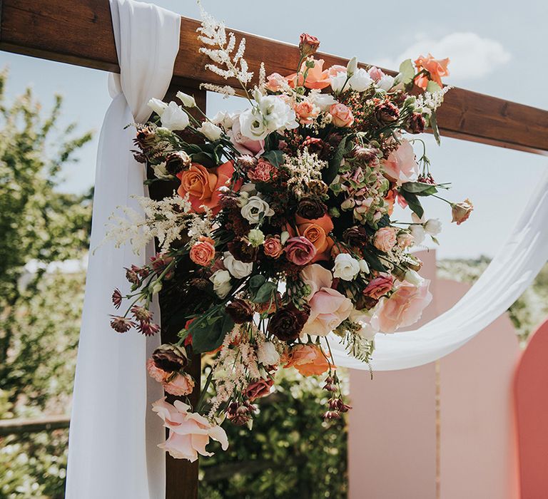 Pink and white wedding flowers on the handmade wooden arch with white drapes with pink wedding screen background