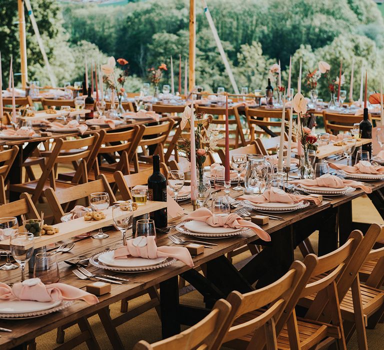 Pink napkins with pink taper candles and coloured glassware decorate the banquet tables for a marquee wedding 