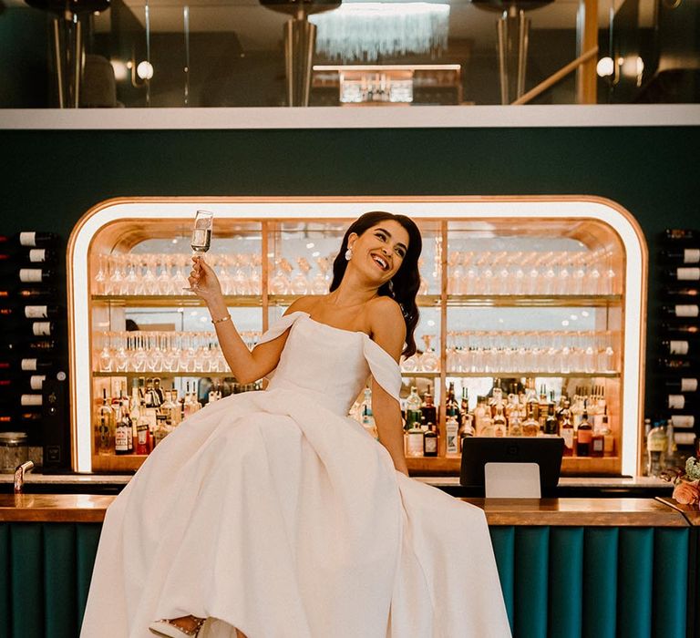 Bride lounges back on the bar with a glass of champagne in her hand