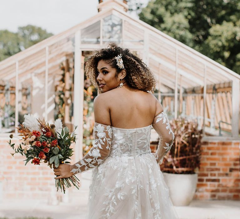 Black bride in a off the shoulder lace and sequin wedding dress with pearl and gold hair clips and earrings at her glasshouse reception 