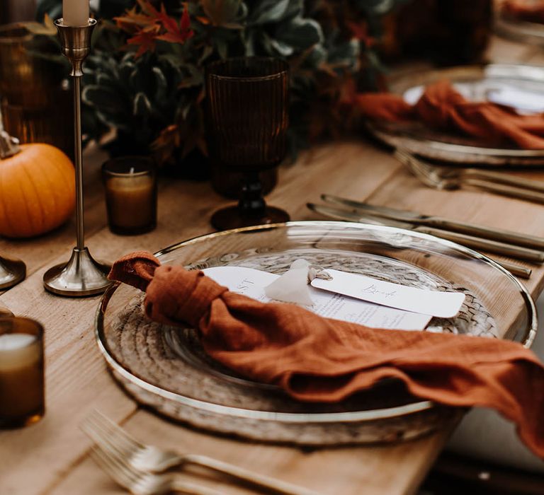 Gold rimmed clear charger plates with orange napkins and wicker placemats with pumpkin decor 