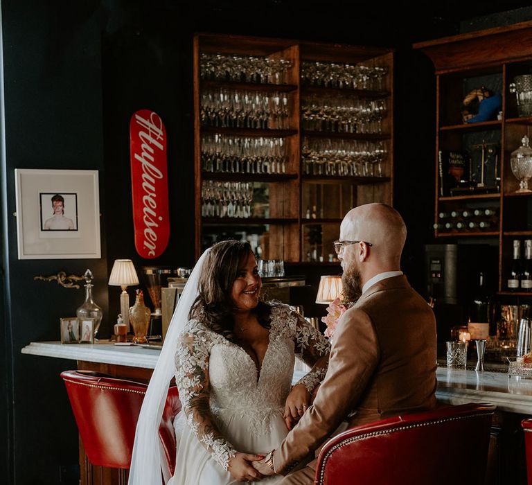 Bride in lace wedding dress sits with her groom at the bar during reception