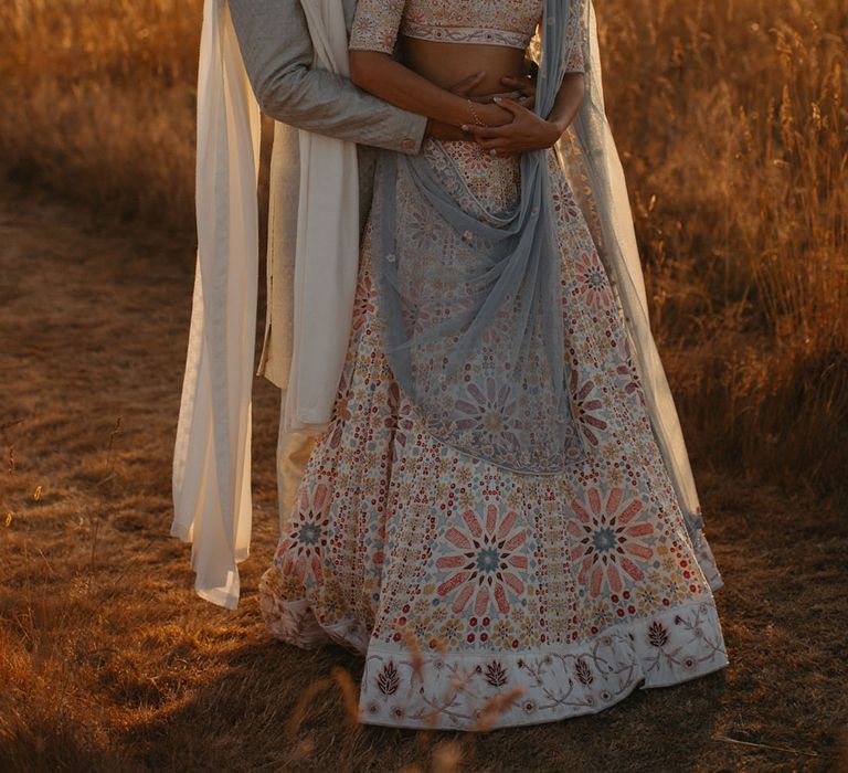 Groom embraces his bride who wears pastel lehenga complete with statement necklace 