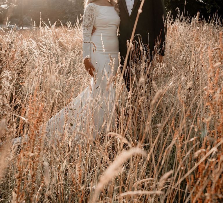 Bride and groom stand in a field together during golden hour for a cute couple portrait 