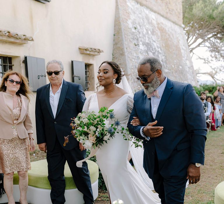 Bride holds father's arm and walks towards the alter in her sheer-sleeved wedding dress and something blue wedding shoes by Manolo Blahnik