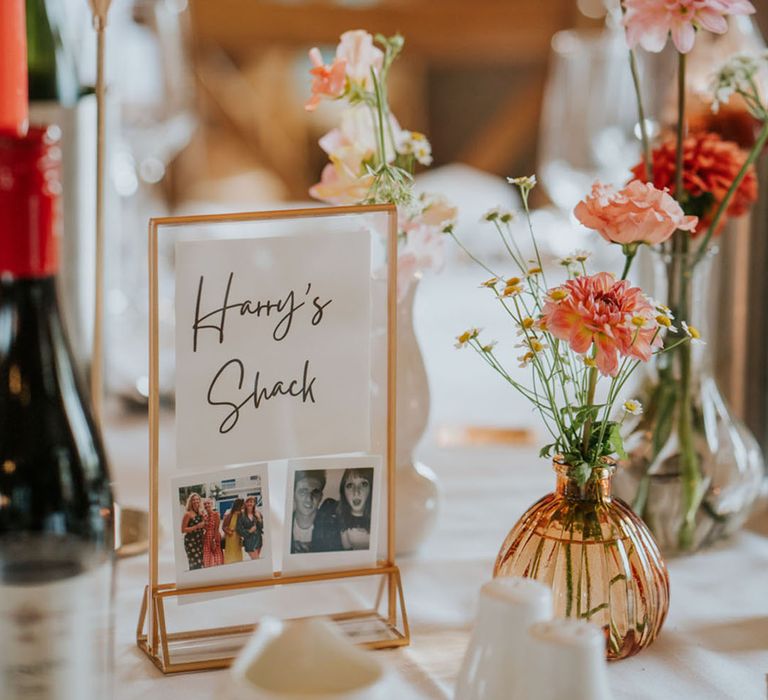 The wedding table with a gold photo frame for the table name and peach and coral taper candles and flowers in bud vases 