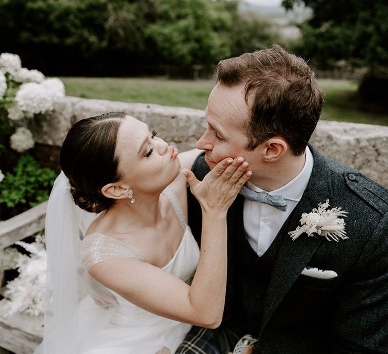 The bride with classic French tip nails turns the groom's face towards her and pouts for a kiss 