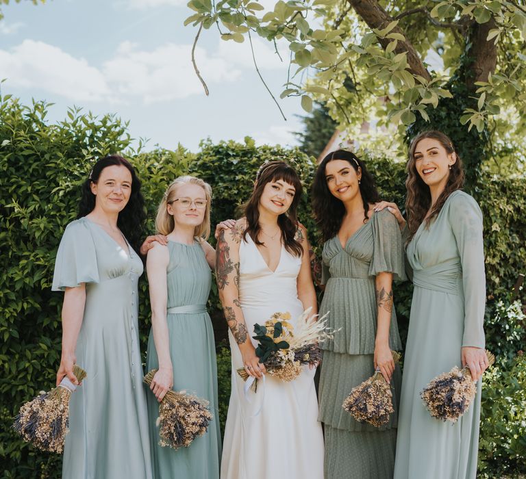 Bridal party in mismatched bridesmaid dresses - sage green and baby blue bridesmaid dresses, all holding dried flower bouquets 