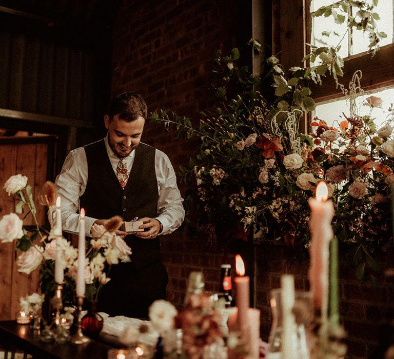 Groom in dark waistcoat with flower patterned tie giving wedding speech at The Giraffe Shed with tapered candles, gold candlestick holders and rose and carnation decorations