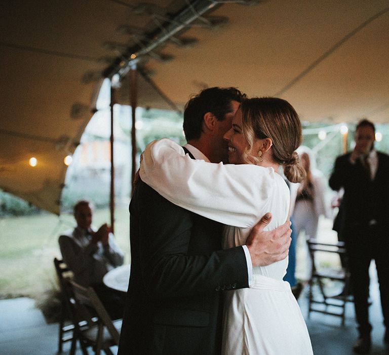 Bride in long sleeve wedding dress lovingly embraces her husband during intimate wedding reception 