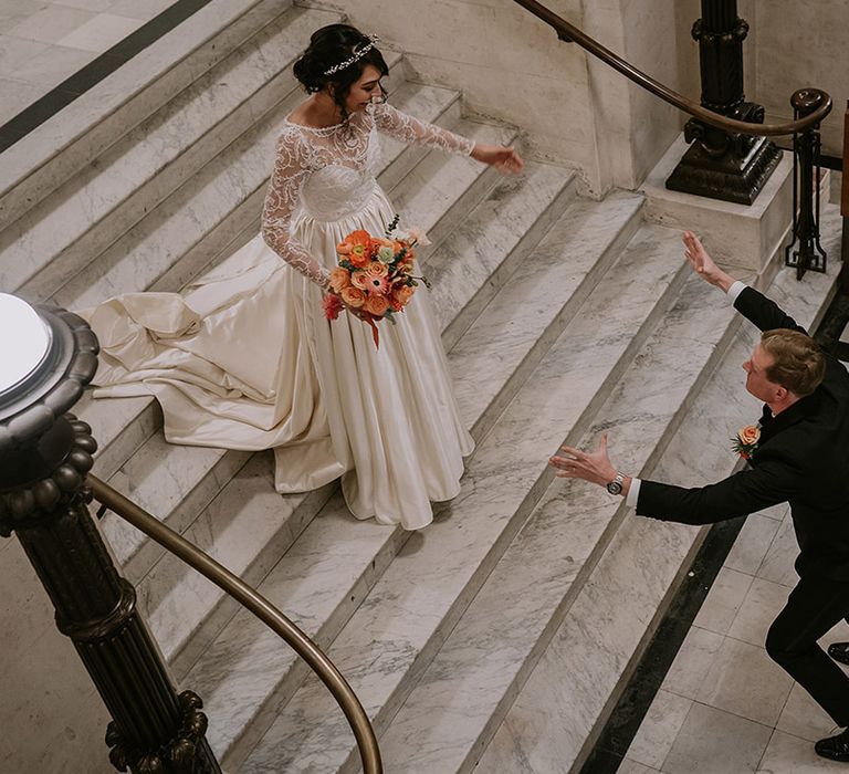 Groom running toward bride with open arms, bride wearing taffeta material princess wedding dress with long lace sleeves 