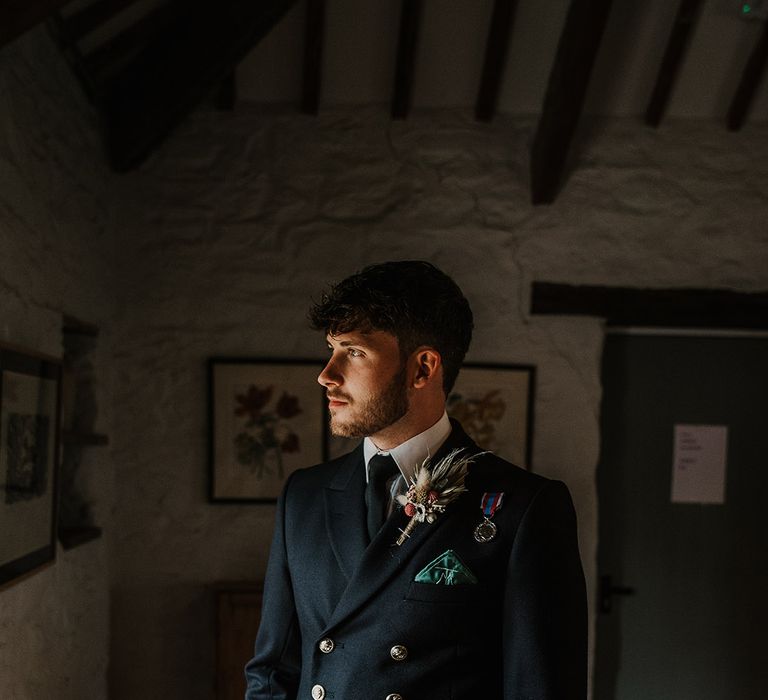 Groom in double breasted military uniform with a dark green pocket square and gold buttons 