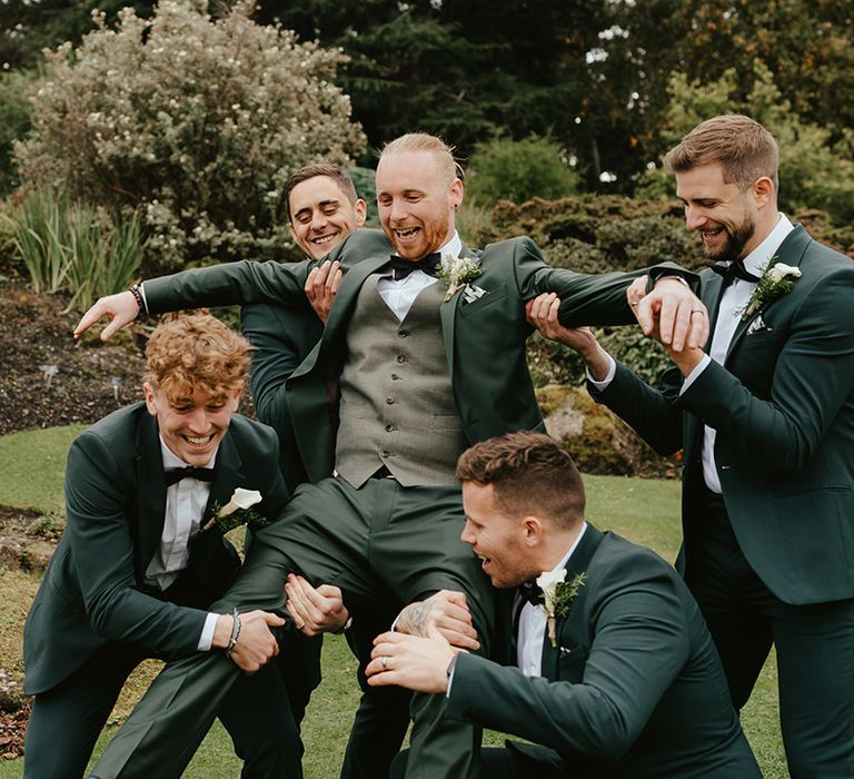 Groomsmen in green suits lift groom after wedding ceremony 