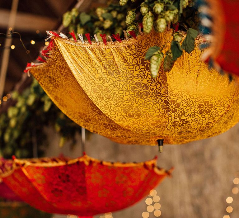 Colourful Indian umbrella wedding decor hangs above tables at Longbourn Estate Barn