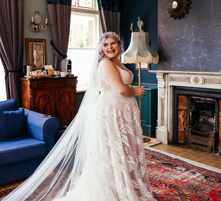 Bride wearing leaf appliqué sheer Evie Young bridal gown and cathedral length veil, smiling at London wedding venue 