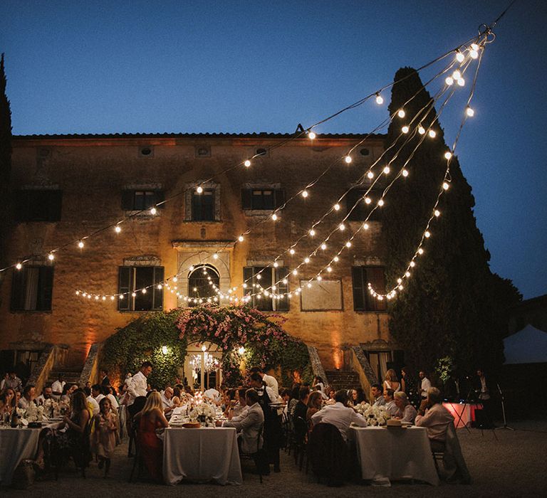 Festoon lighting hangs above banquet tables for outdoor wedding ceremony in the Tuscan countryside at Villa Di Ulignano 