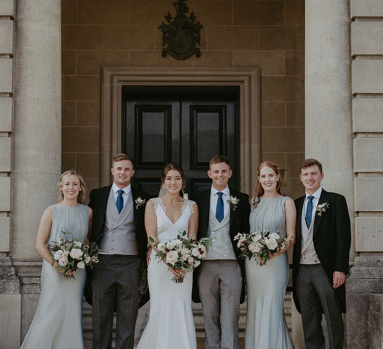 Bride & groom stand alongside their bridesmaids in sage green bridesmaid dresses and groomsmen in Morning suits