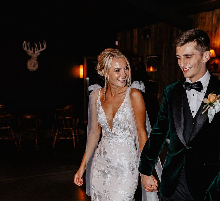 Flash photo of the bride walking her fitted wedding dress with detachable tulle wings with the groom in a green velvet tuxedo 