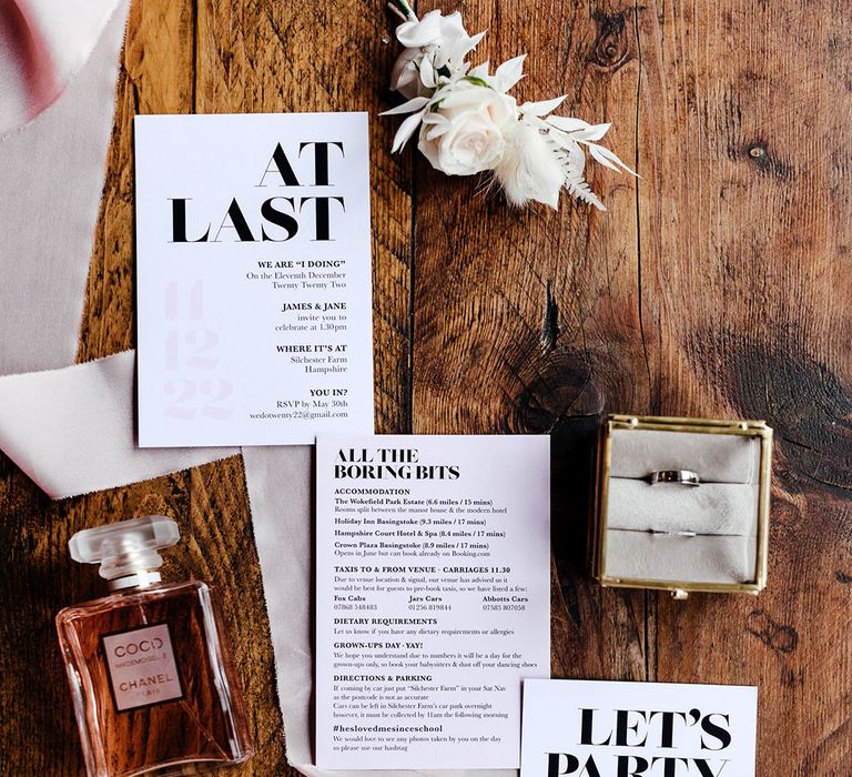 Black and white wedding stationery with Chanel perfume, pink ribbon, the wedding rings, and a buttonhole flower accessory 