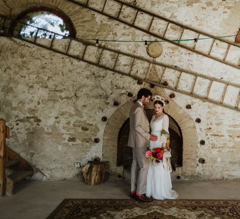 Bride and groom at rustic wedding venue in italy wearing a white lace wedding dress, boho bridal crown, and greige groom's suit