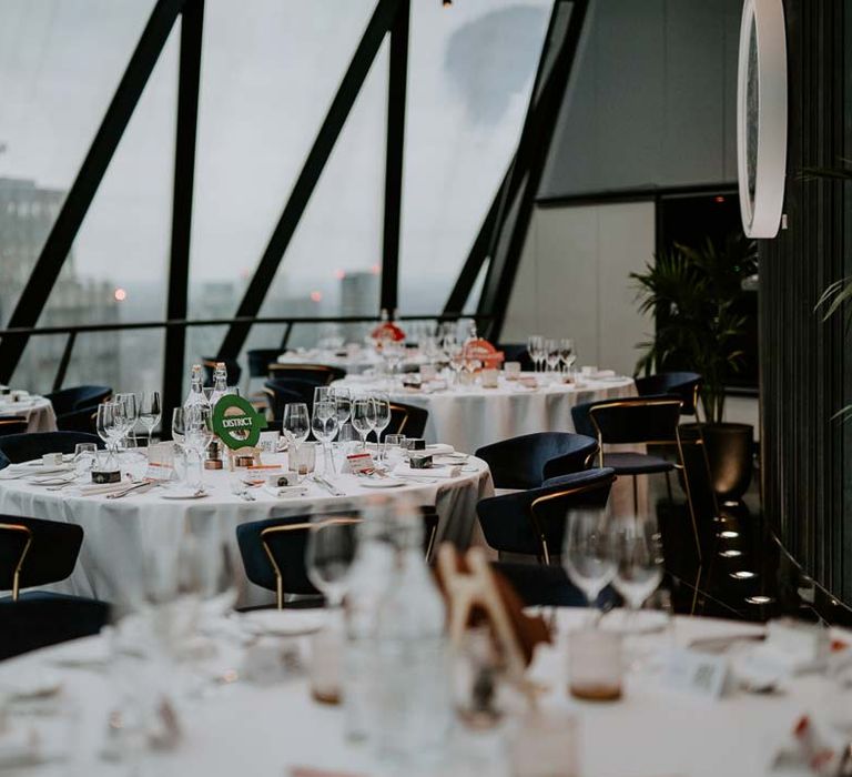 Classic wedding tablescapes with white tablecloth, tube station table numbers and black chairs with golden rims at The Gherkin wedding venue 