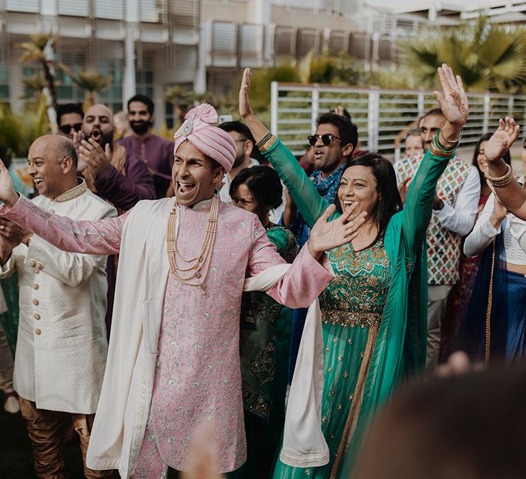 Wedding guests dancing with groom in light pink sherwani, light pink shoes and light pink turban and cream trousers  