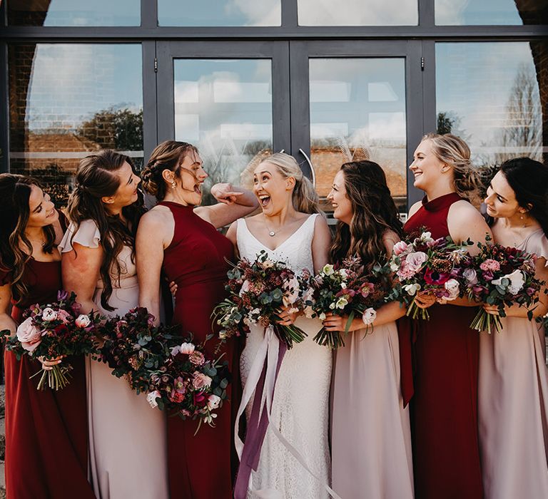 Bridesmaids in mismatched red and pink bridesmaid dresses with the bride in a fitted floral lace wedding dress 