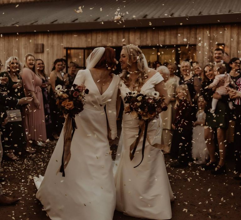 Bride in satin short sleeve deep v wedding dress and church length veil and bride in long sleeve deep v wedding dress and church length veil doing dried petal confetti exit 