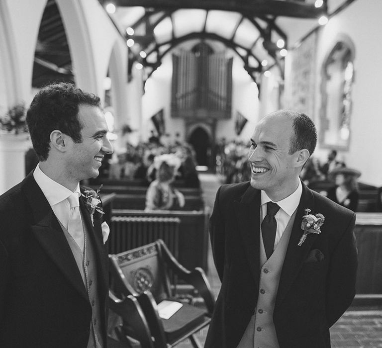 The groom and best man smile together as they nervously wait for the bride 