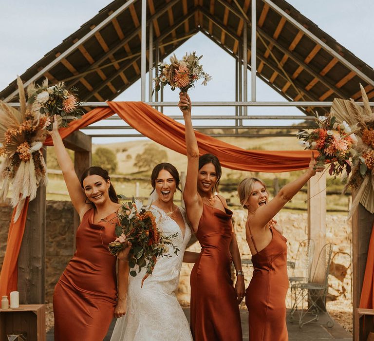 Epic bridal party wedding photo with the bride and bridesmaids raising their bouquets in the air for orange theme wedding 