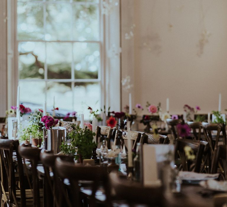 Bud vases with colourful wedding flowers alongside white candles in gold candleholders decorate the wedding tablescape 