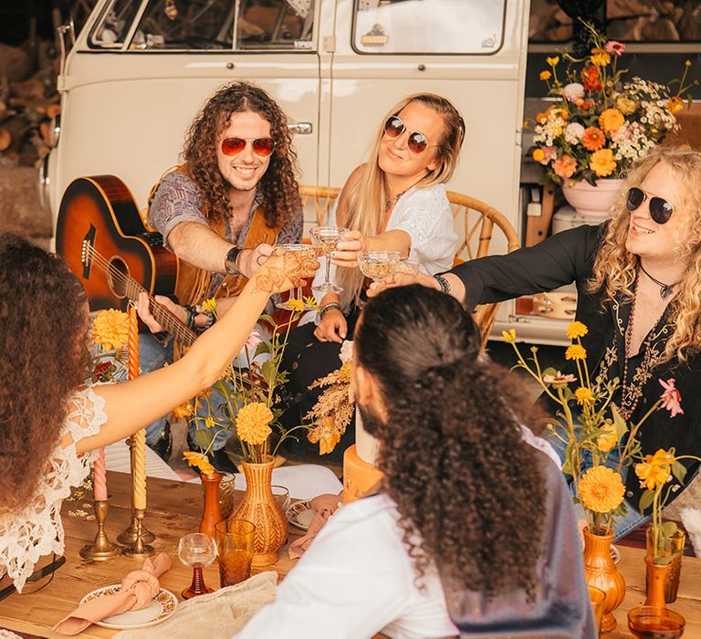 Wedding guests and musicians sit around an orange wedding table for vintage wedding inspired by Woodstock 