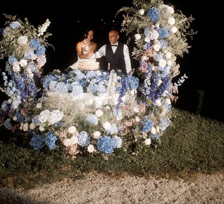 White and blue wedding flower arrangements surround the wedding cake