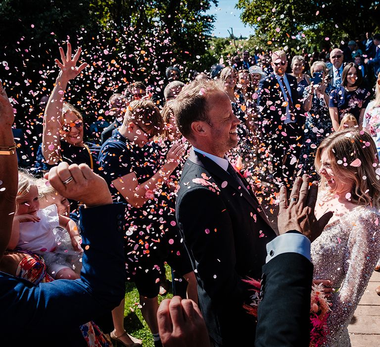 The bride and groom have colourful confetti exit at outdoor wedding ceremony 