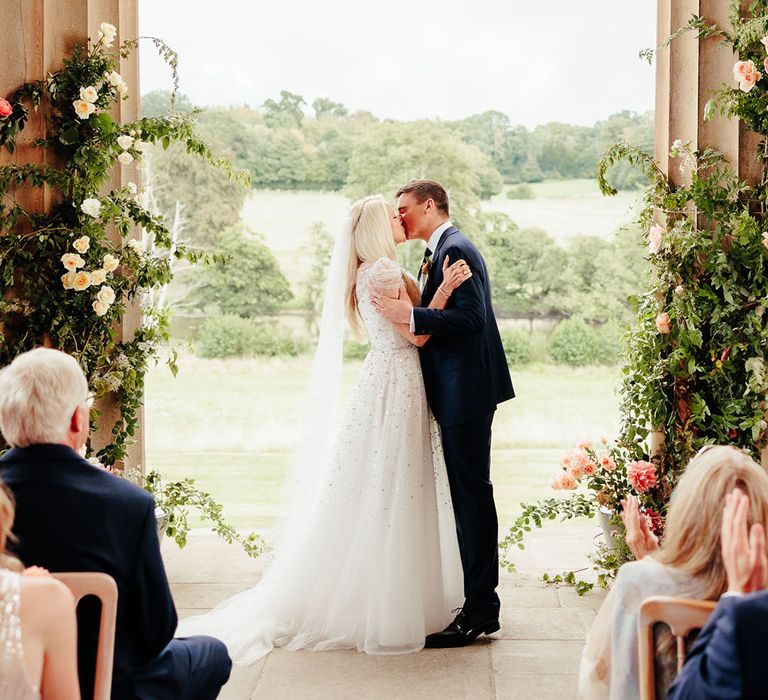 The bride and groom share their first kiss as a married couple at their outdoor wedding ceremony 